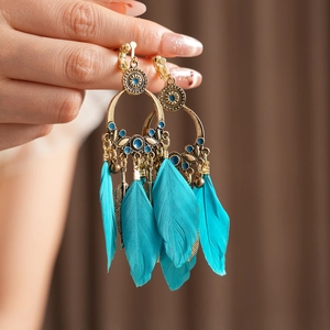 Détail de boucles d'oreilles bohèmes dorées avec pierres bleues et pompons plumes