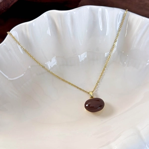 Macro shot of gold necklace with red bean pendant on a white shell tray