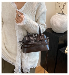 Detail of a dark brown glossy leather shell bag with metallic buckle and shoulder strap