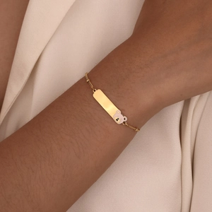 Detailed view of an 18K gold-plated ID bracelet with a pink bear charm on a wrist