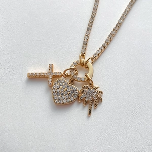 Dettaglio macro della collana placcata oro 14K con ciondoli a cuore, croce e palma