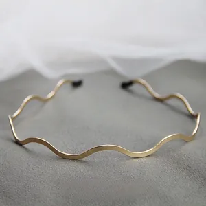 Dettaglio di un elegante cerchietto metallico ondulato dorato su sfondo materico