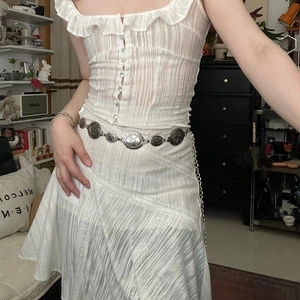 Detail eines Vintage-Metallgürtels mit ovaler Textur auf weißem Rüschenkleid
