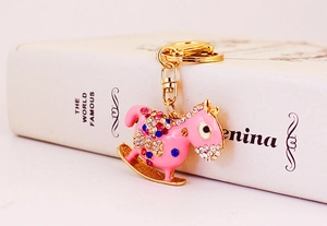 Detail view of a pink rocking horse keychain with colorful rhinestones on a gold base
