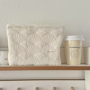Cream quilted shell makeup bag with brand label on a minimalist wooden shelf display