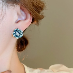 Macro detail of blue enamel flower earring with pearl and diamonds on model ear