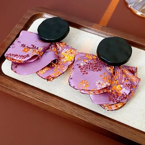 Detail of purple floral fabric earrings with black studs on a wooden tray background