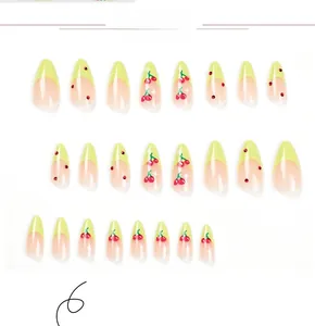 Detail of almond-shaped press-on nails with green French tips and red cherry accents