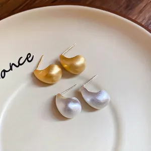 Minimalist brushed metal teardrop earrings in gold and silver plating on a ceramic tray