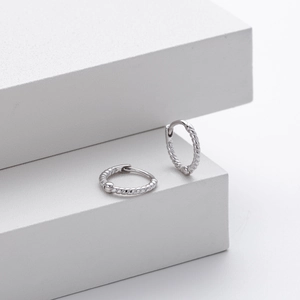 Macro view of silver twisted hoop earrings on white geometric stands for modern jewelry display