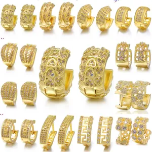 Macro shot of gold huggie earrings set with zircon featuring heart and leaf designs