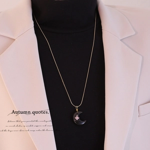 Dettaglio della collana con ciondolo a mezzaluna indossata su un lupetto nero chic