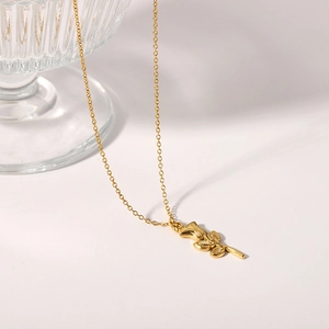 18K gold plated 3D rose pendant necklace draped on glass over light beige background