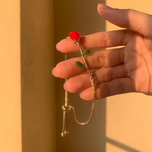 Detail showing an adjustable gold rose bracelet with red flower and green leaf charms
