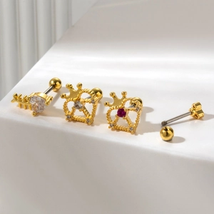 Golden stainless steel cartilage studs set with heart, crown, and zircon stones on white surface