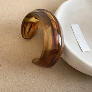 Macro detail of amber acrylic cuff bracelet with brown marble texture and wide C-shape