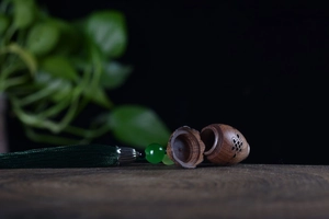 Detailed carved wood sachet pendant with green jade bead and silk tassel on wood surface
