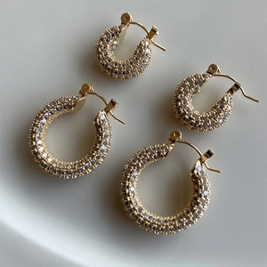 Golden U-shaped zircon hoop earrings set with sparkling stones on minimalist off-white base