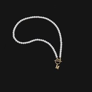 Detailed close-up of pearl necklace featuring a gold OT toggle clasp and letter M pendant