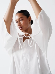Loose white cotton V-neck dress with wavy trim and tassel ties for a casual summer style