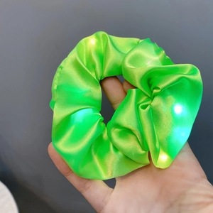 Close-up of hand holding a neon green LED scrunchie with glowing lights and satin texture