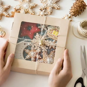 Hands holding a kraft paper gift box with Christmas gingerbread cookies and twine