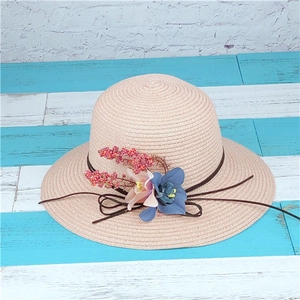 Dettaglio di un cappello di paglia rosa con decorazioni floreali di fiori blu e rosa