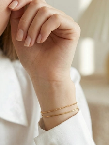 Close-up of layered gold double chain bracelet featuring a snake and bead chain design