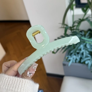 Detail of light green butterfly claw clip with golden metal spring and non-slip teeth