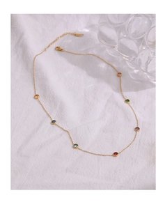 Detail of a thin gold necklace with multi-colored round zircon gemstones on white fabric