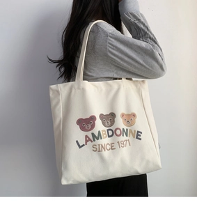 Close-up of model carrying off-white canvas tote with embroidered bears and logo