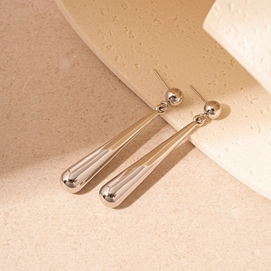 Macro detail of silver drop earrings with a polished metallic finish on beige stone