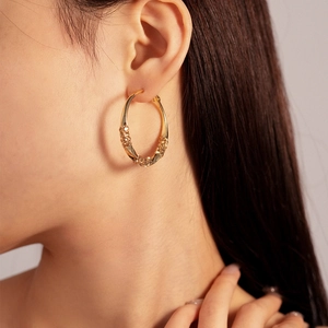 Close-up of golden geometric hoop earrings with twisted texture and sparkling crystals