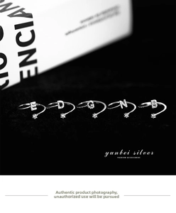 Detailed shot of five adjustable silver letter rings with sparkling crystals on black velvet