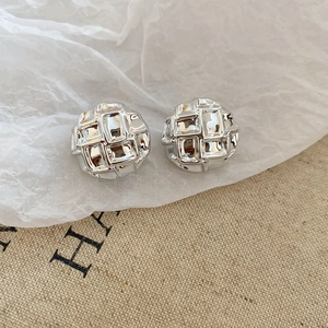 Detail of round silver metallic stud earrings featuring quilted checkerboard texture