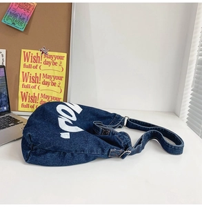 Detail of dark blue denim crossbody bag with large white letter print on a desk