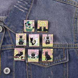 Detailed view of eight black cat tarot enamel pins attached to a denim jacket collar