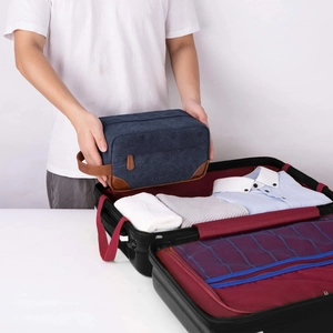 Navy blue canvas toiletry bag being packed into a travel suitcase for organization