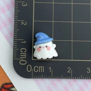 Close-up of mini white ghost resin charm with blue hat on a measuring grid mat