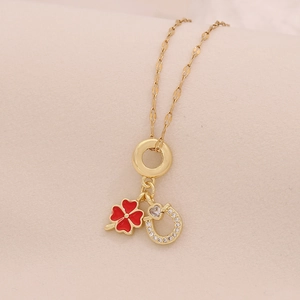 Detail of gold necklace with red four-leaf clover and crystal horseshoe pendant