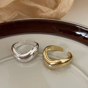 Close-up of minimalist wave-shaped 925 silver rings in silver and gold on a ceramic plate
