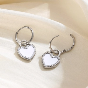 Silver stainless steel heart earrings with white enamel finish on cream fabric background