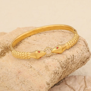 Macro shot of gold snake bracelet with red gemstone eyes resting on a natural beige stone