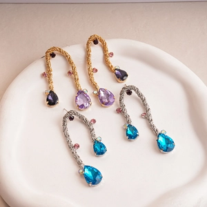 Metallic woven teardrop earrings with purple and blue gems on a ceramic tray