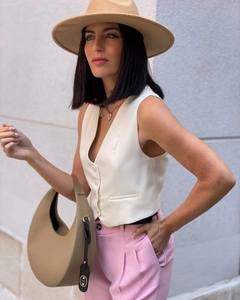 Femme en gilet blanc, pantalon rose, chapeau fedora et sac à main beige en extérieur