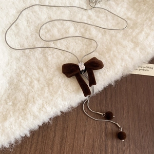 Detail of zircon velvet bow necklace with pompons on white fleece and wooden desk