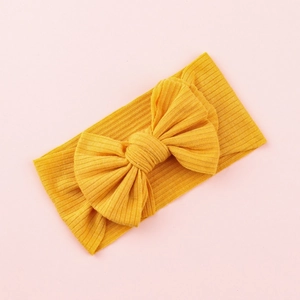 Yellow ribbed knit baby headband with a large bow displayed on a soft pink background