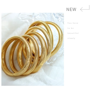 Detailed close-up of golden spiral snake bone textured bangles stacked on white fabric