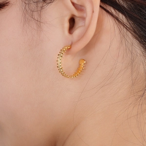 Close-up of golden C-shaped fishbone textured earrings worn on a female model's ear