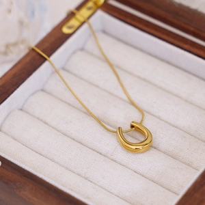 Minimalist gold titanium steel U-shaped horseshoe necklace on a wooden jewelry box